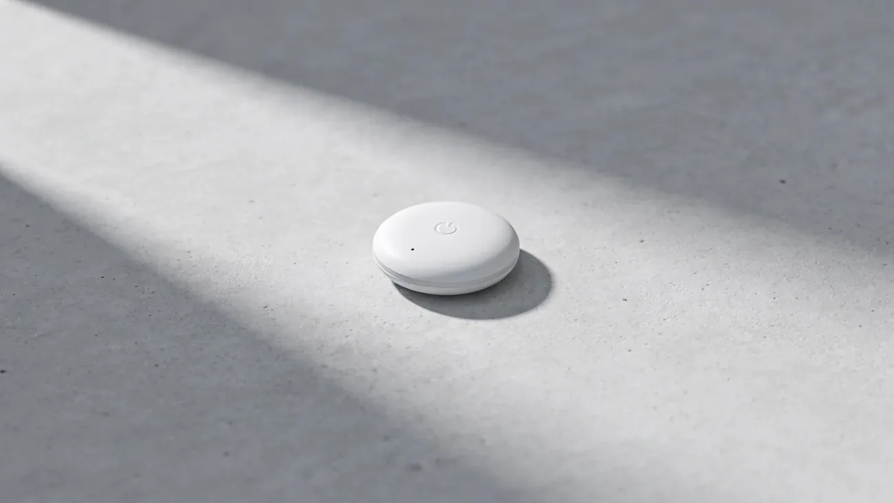 Small white Bluetooth tracker alone on a light grey concrete surface, long natural shadow