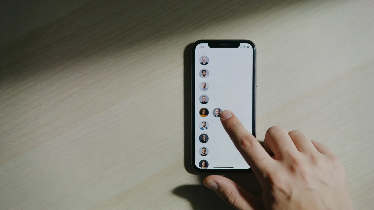 Tela de iPhone com aplicativo Buscar aberto, lista de membros familiares com um nome em foco e botão Parar de Compartilhar Minha Localização visível, mãos segurando o aparelho